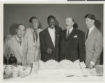 Photograph of Nat King Cole with a group of men around a birthday cake shaped like a crown