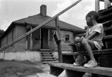 Negro boy sitting on steps outside big house.