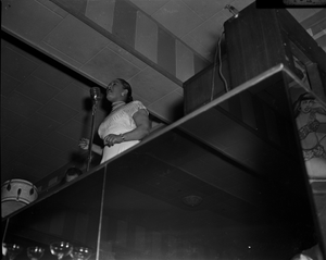 Billie Holiday [onstage, singing at microphone, looking up at stage from a low angle] [cellulose acetate photonegative]