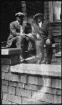Two men in suits and hats sitting on front porch steps