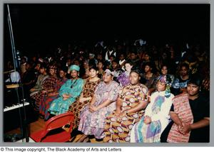 Photograph of a row of women and a crowd of people behind them