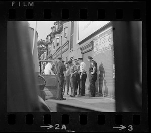 Police standing outside of a patrol car and speaking with a group of young Black men on the sidewalk, most likely after unrest broke out during student demonstrations