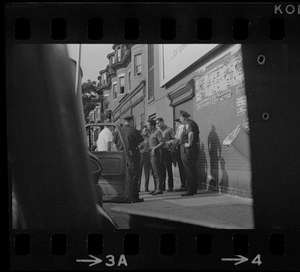 Police standing outside of a patrol car and speaking with a group of young Black men on the sidewalk, most likely during time of student demonstrations at nearby high schools