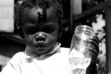 Small child holding a glass jar on the porch of a house in Newtown, a neighborhood in Montgomery, Alabama.