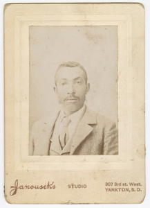 Photograph of a man wearing a light colored jacket, vest and necktie