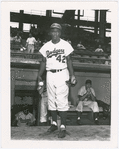 Brooklyn Dodgers infielder Jackie Robinson outside the team's dugout at Ebbets Field, Brooklyn, New York, with centerfielder Duke Snider (at left in dugout) and pitcher Preacher Roe (sitting at right in dugout), circa 1950