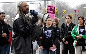 Thumbnail for Justice for Jason rally at UMass Amherst: Amilcar Shabazz, Chair of UMass Afro-American Studies, speaks near a flower-filled fence, to students and staff who rally in support of Jason Vassell