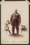 [Full-length portrait of an African American veteran and GAR member, standing on rug between table and chair]