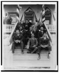 [Booker T. Washington, seated on steps, with group of other men, outside of building]