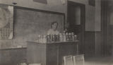 African American woman, probably a teacher, seated behind a desk in a classroom in rural Jefferson County, Alabama.