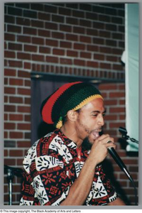 Photograph of the left profile side of a man rapping into a microphone