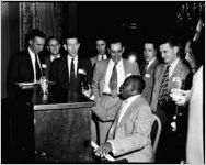 Company executives around up-right piano, with African-American keyboard player holding Coca-Cola bottle. Coca-Cola Company party at the Capitol City Club, Atlanta, Georgia, March 18, 1954