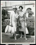 African American woman wearing hat and carryng two hat boxes posing with another woman, Los Angeles, ca. 1951-1960