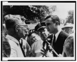 A police officer listens as Nashville's Superintendent of City Parks, F.W. Perkins (left), informs segregationist John Kasper (right), that he cannot hold a rally in Centenial [sic] Park without a permit [...]