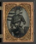 [Sergeant Albert S. Brownson of Company G, 12th Indiana Infantry Regiment, and Company D, 5th Indiana Cavalry Regiment, in uniform and upside down U.S. belt buckle with revolver in front of American flag backdrop]