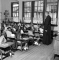 Priest calling on students with their hands raised in a classroom at Nazareth Catholic Mission in Montgomery, Alabama.