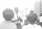 Dan Houser speaking to a group of people standing outside a brick church building in Prattville, Alabama, during a meeting of the Autauga County Improvement Association.