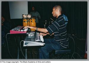 Photograph of a man playing two different kind of keyboards