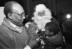 Rev. H.H. Brookins with Tom Bradley in a Santa suit talking to a child, Los Angeles, 1982