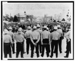 Helmeted state conservation department agents stand on capitol steps and watch 30,000 civil rights demonstrators conduct ceremonies and speeches in front of them