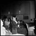 [Store Front Churches. A woman seated with her hands clasped while others around her clap and raise their hands at Elder Beck's Church, Genesee St., Buffalo, N.Y.]