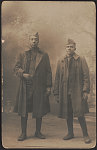 [Two unidentified African American soldiers in uniforms, greatcoats, and overseas caps in front of painted backdrop]