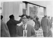 Mississippi State Sovereignty Commission photograph of an unidentified white male holding a photograph of an African American adult and child at an Anti-Vietnam War protest held during Secretary of Defense Robert McNamara's visit to Jackson, Mississippi, 1967 February 24