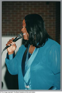 Photograph of a woman singing into a microphone facing towards the left