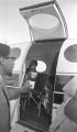 Richard Boone holding a paper cup outside the open door of a plane at the airport in Montgomery, Alabama.