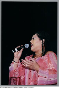 Angela Bofill singing with her left hand up