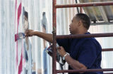 Lorenzo Green painting a patriotic mural on the side of Lambert's Cafe on Highway 59 in Foley, Alabama.