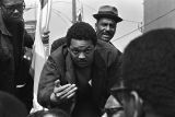 Jesse Jackson motioning to someone while riding on the cart carrying Martin Luther King, Jr.'s casket during the funeral procession.