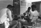 Four young men playing cards on the front porch of a clapboard house in Newtown, a neighborhood in Montgomery, Alabama.