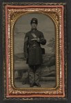 [Unidentified soldier in Union sergeant's uniform standing with revolver and cartridge box in front of painted backdrop showing countryside landscape]