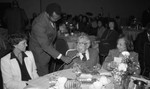 Dr. H. Claude Hudson sitting at a table as he speaks into a microphone, Los Angeles, 1983