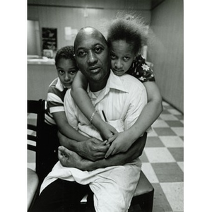 Young girl and boy hug seated man.