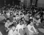 Large group of mostly African-American and Asian-American school children seated on the floor of an unidentified room, Seattle, 1951