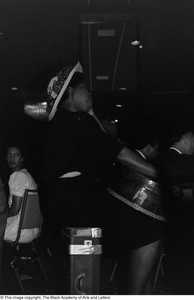 Photograph of a woman holding a drum while sitting on a suitcase