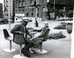 Old couple chatting at sidewalk table across from the Morrison Hotel, 3rd ave. and Jefferson St., circa 1966