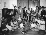 Women and children seated around the piano at the Fannie Wall Children’s Home and Day Nursery