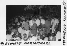 Mississippi State Sovereignty Commission photograph of Stokely Carmichael being interviewed by an unidentified white male in the center of a large crowd at an outdoor gathering, Tougaloo, Mississippi, 1960s