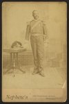 [African American soldier, full-length portrait, wearing GAR medal, standing next to table]