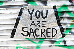 "You are Sacred," sign on the entrance to Little Skips coffe shop, "a space that uplifts the voices that have been silenced for so many years."  The sign is surrounded by stickers with the names of Blacks killed by the police. Myrtle Ave. at Charles Pl., Brooklyn