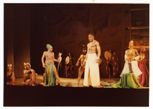 Performance picture of Eartha Kitt (standing, green turban, on the left), tall man in white, and many cast members]. [color photoprint