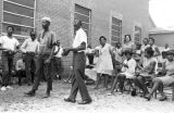 Thumbnail for Dan Houser and another man, standing in front of an audience outside a brick church building in Prattville, Alabama, during a meeting of the Autauga County Improvement Association.