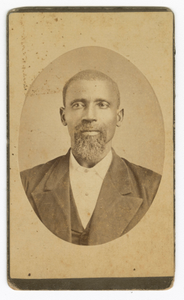 Photograph of a man with a beard wearing a dark colored suit and vest