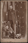 [Civil War veteran and amputee Henry A. Seaverns of G.A.R. George W. Perry Post no. 31, Scituate, Massachusetts, in uniform with sword, canteen, and other artifacts, standing on crutches in front of American flag]