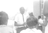 Dan Houser speaking to a group of people standing outside a brick church building in Prattville, Alabama, during a meeting of the Autauga County Improvement Association.