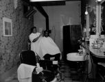 African-American barber cutting the hair of a patron in a local barber shop, ca. 1950's