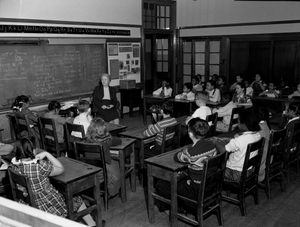 Integrated primary school class and teacher, with notes about manners and math on blackboard, Washington, D.C.] [Black-and-white photonegative.